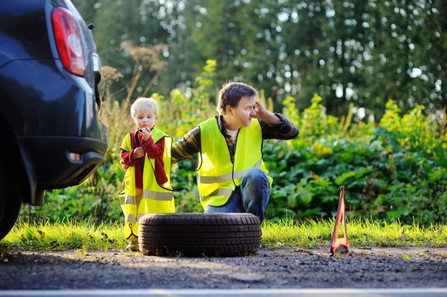 Father with little son repairing car and changing wheel together